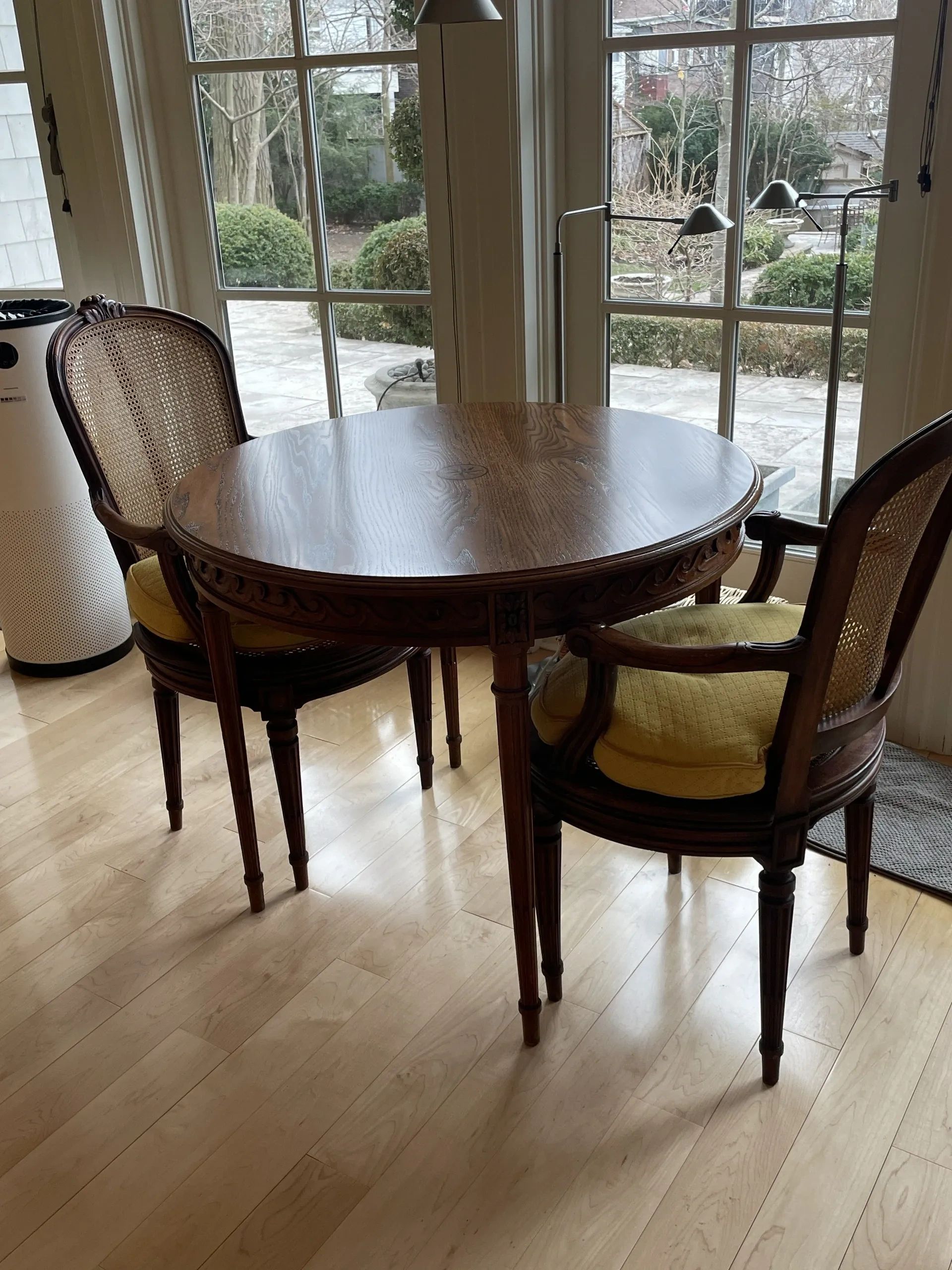 Bright sunlit dining room with round dark wood table and cane-backed chairs